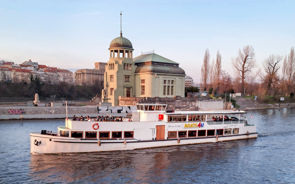 Historic cruise boat on Vltava River passing by a riverside building in Prague.