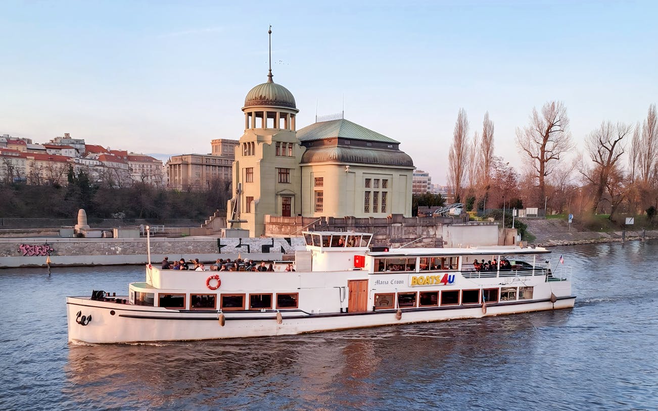 Historic cruise boat on Vltava River passing by a riverside building in Prague.
