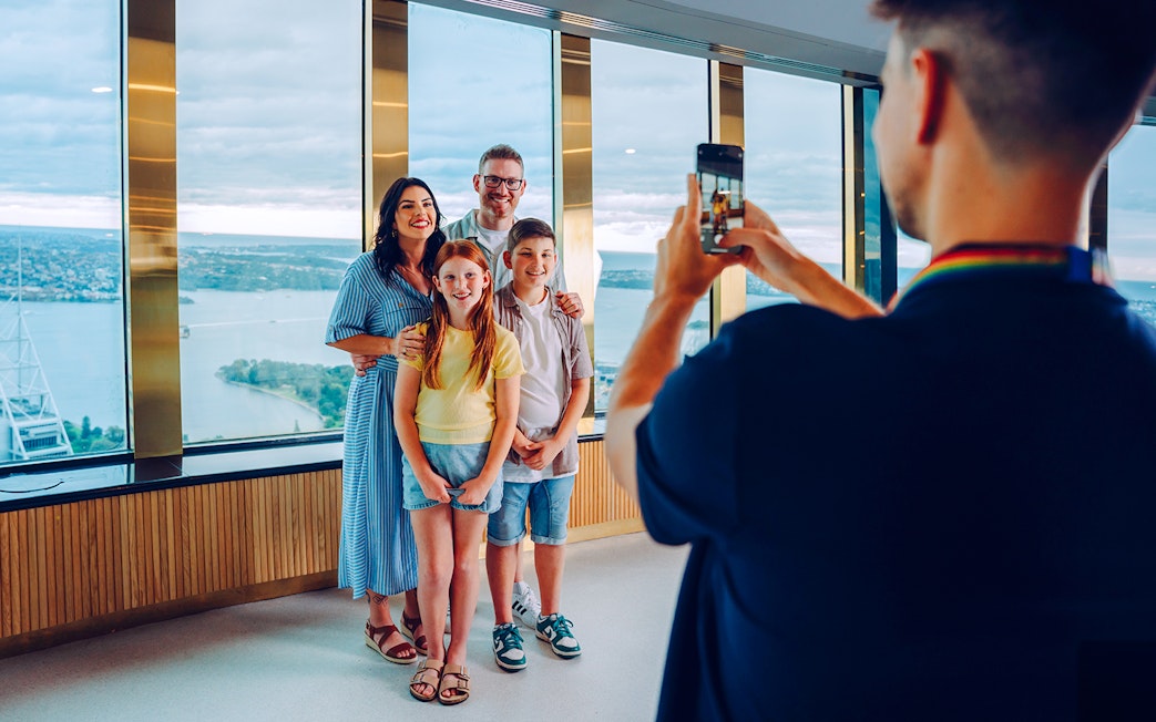 Family posing for a photo at Sydney Tower Eye with city view in background.