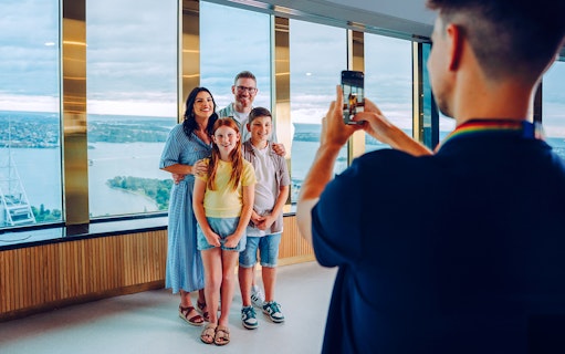 Family posing for a photo at Sydney Tower Eye with city view in background.