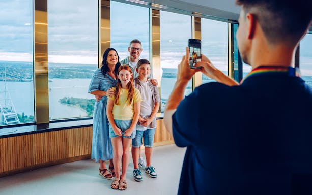 Family posing for a photo at Sydney Tower Eye with city view in background.