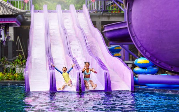 Children sliding down water slides at Toya Devasya Hot Spring Water Park, Bali.