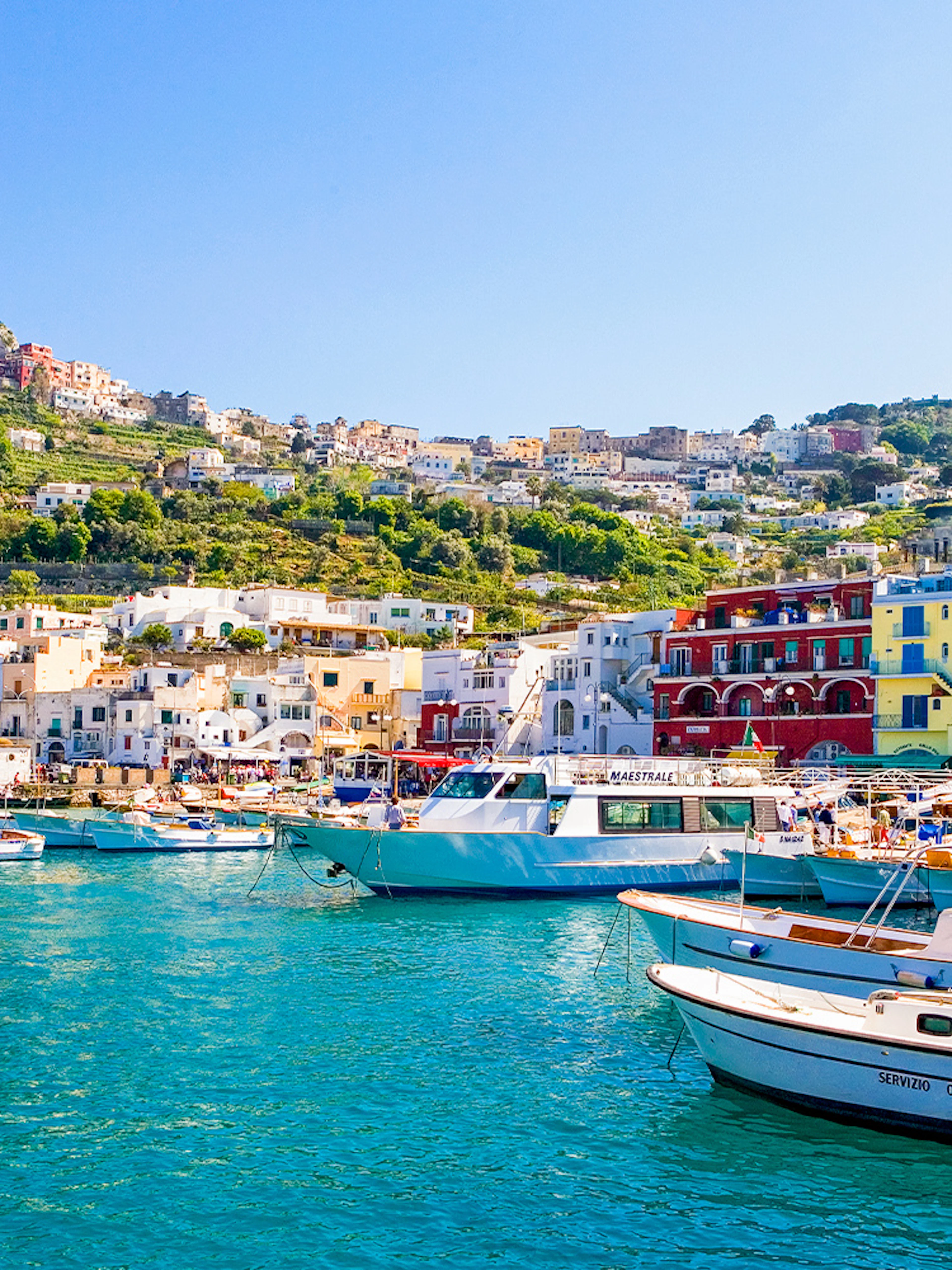 Boats in Marina Grande, Capri, with colorful buildings and cliffs in the background, Italy.