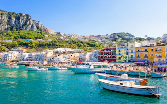 Boats in Marina Grande, Capri, with colorful buildings and cliffs in the background, Italy.
