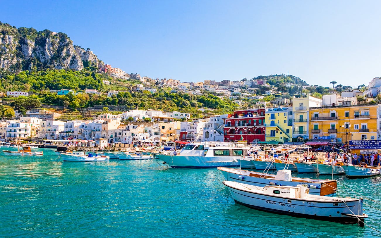 Boats in Marina Grande, Capri, with colorful buildings and cliffs in the background, Italy.