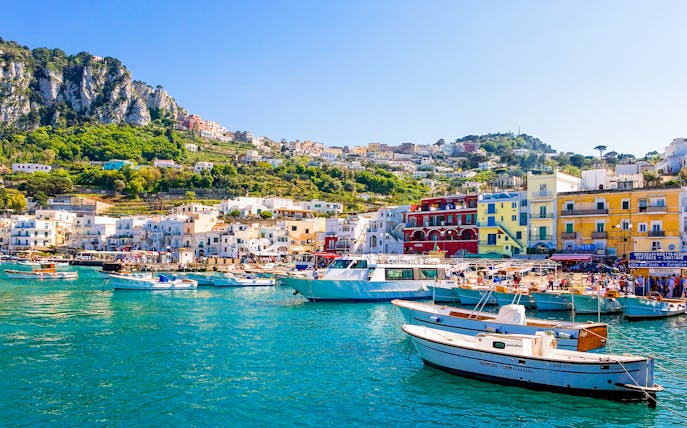 Boats in Marina Grande, Capri, with colorful buildings and cliffs in the background, Italy.