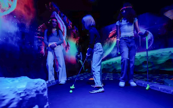 Guests playing mini golf under blacklight with glowing murals.