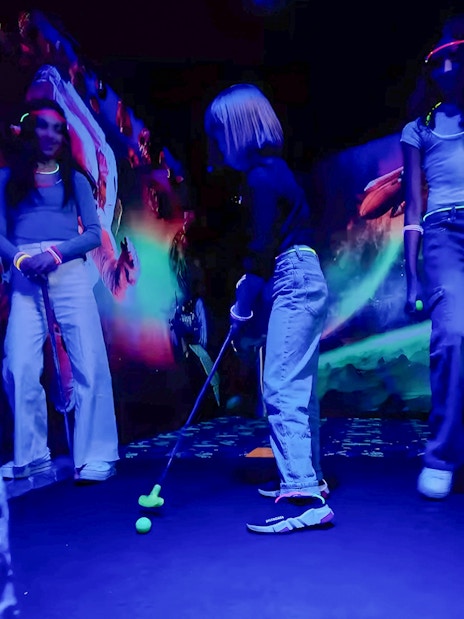 Guests playing mini golf under blacklight with glowing murals.