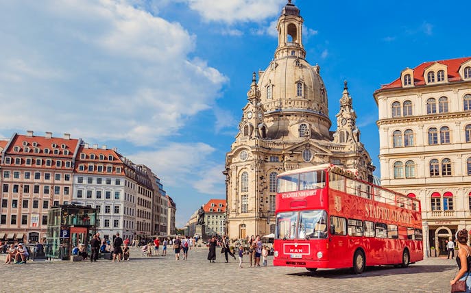 Red double-decker bus in front of Dresden's Frauenkirche during guided city tour.