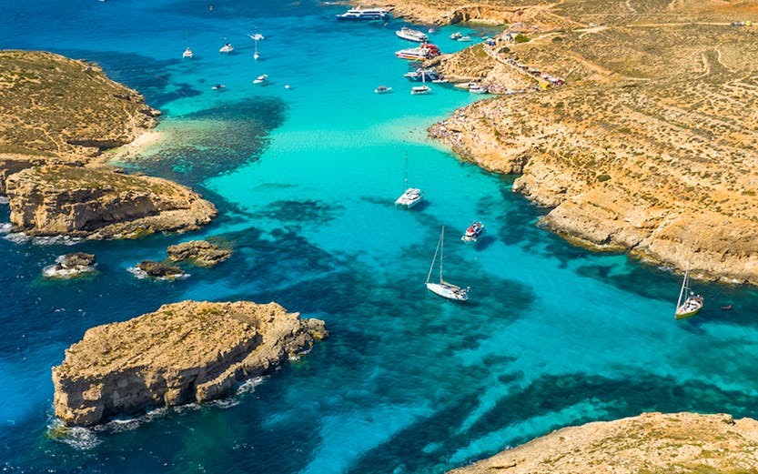 Blue Lagoon on Comino Island with tourists swimming in clear turquoise waters.