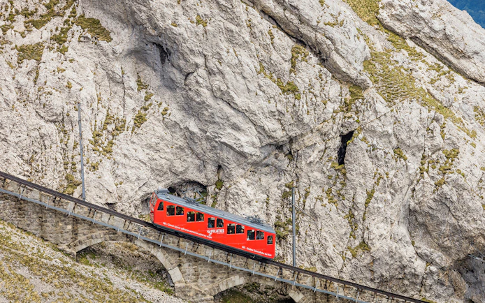 Red cogwheel train ascending Mount Pilatus in Lucerne, part of the Swiss Travel System.