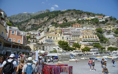 Crowded beach with colorful buildings on hillside in Positano, Amalfi Coast.