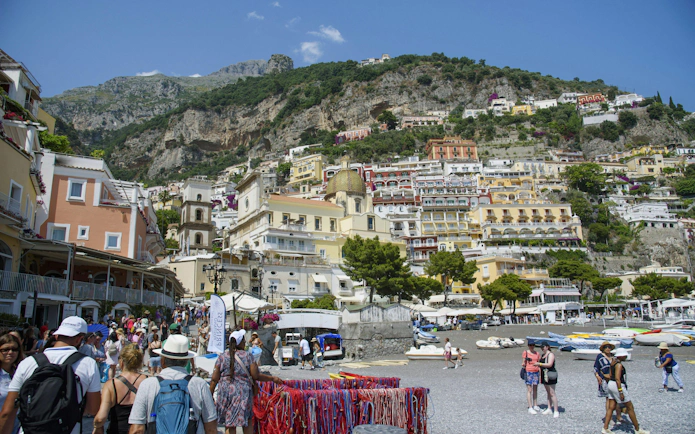 Crowded beach with colorful buildings on hillside in Positano, Amalfi Coast.