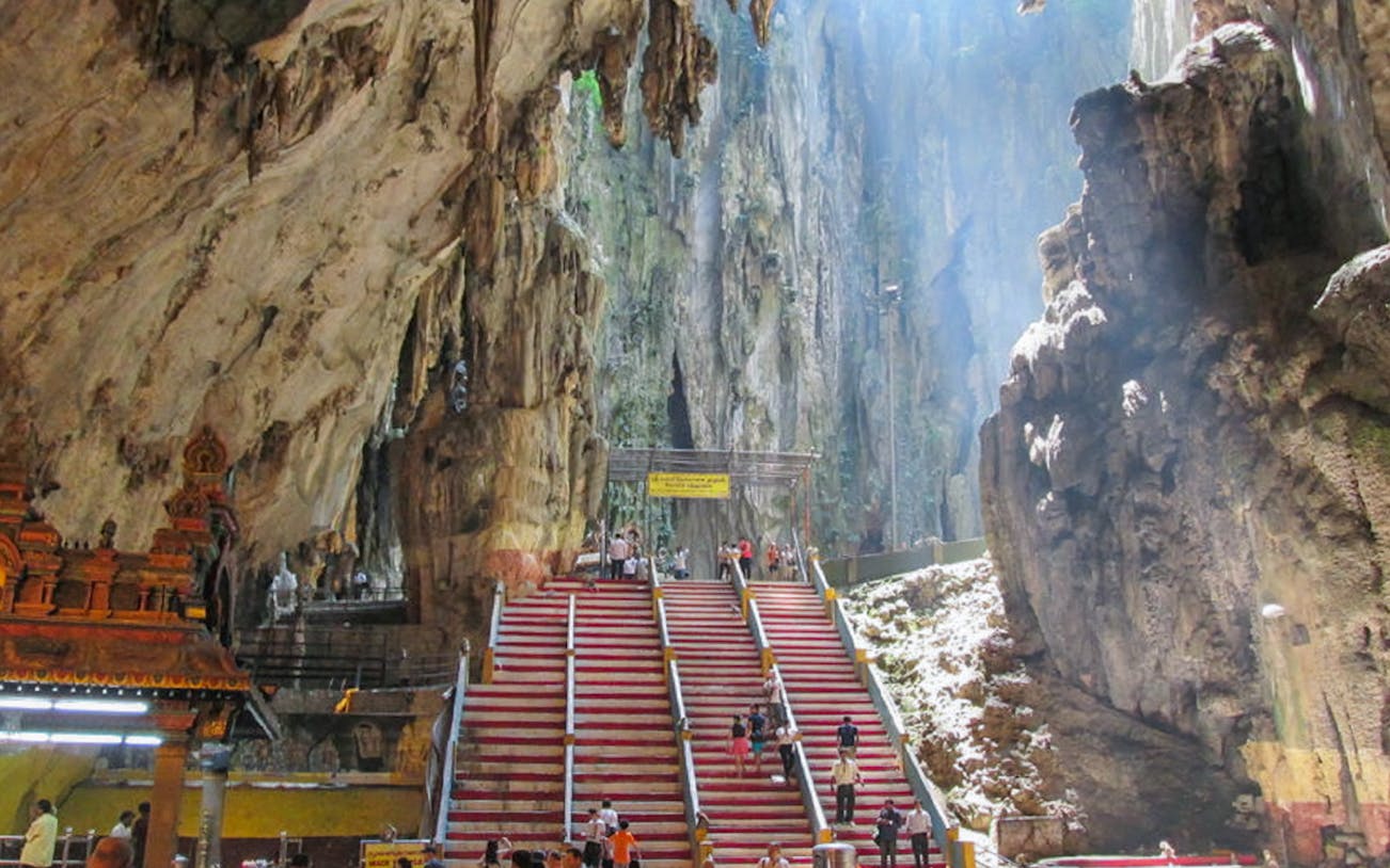 Stairs leading to Batu Caves with visitors ascending, surrounded by limestone formations.