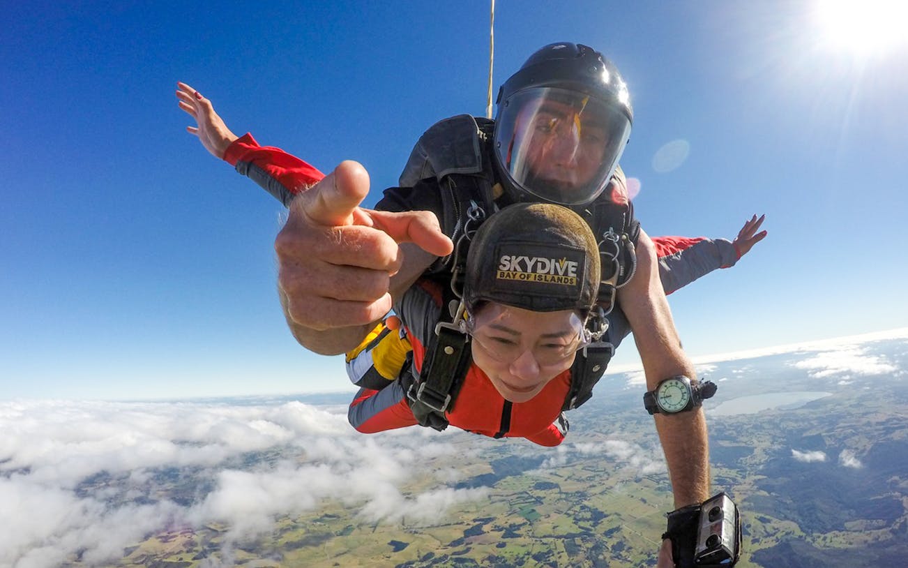 Tandem skydiving over Bay of Islands at 12,000 ft with clear skies and ocean view.