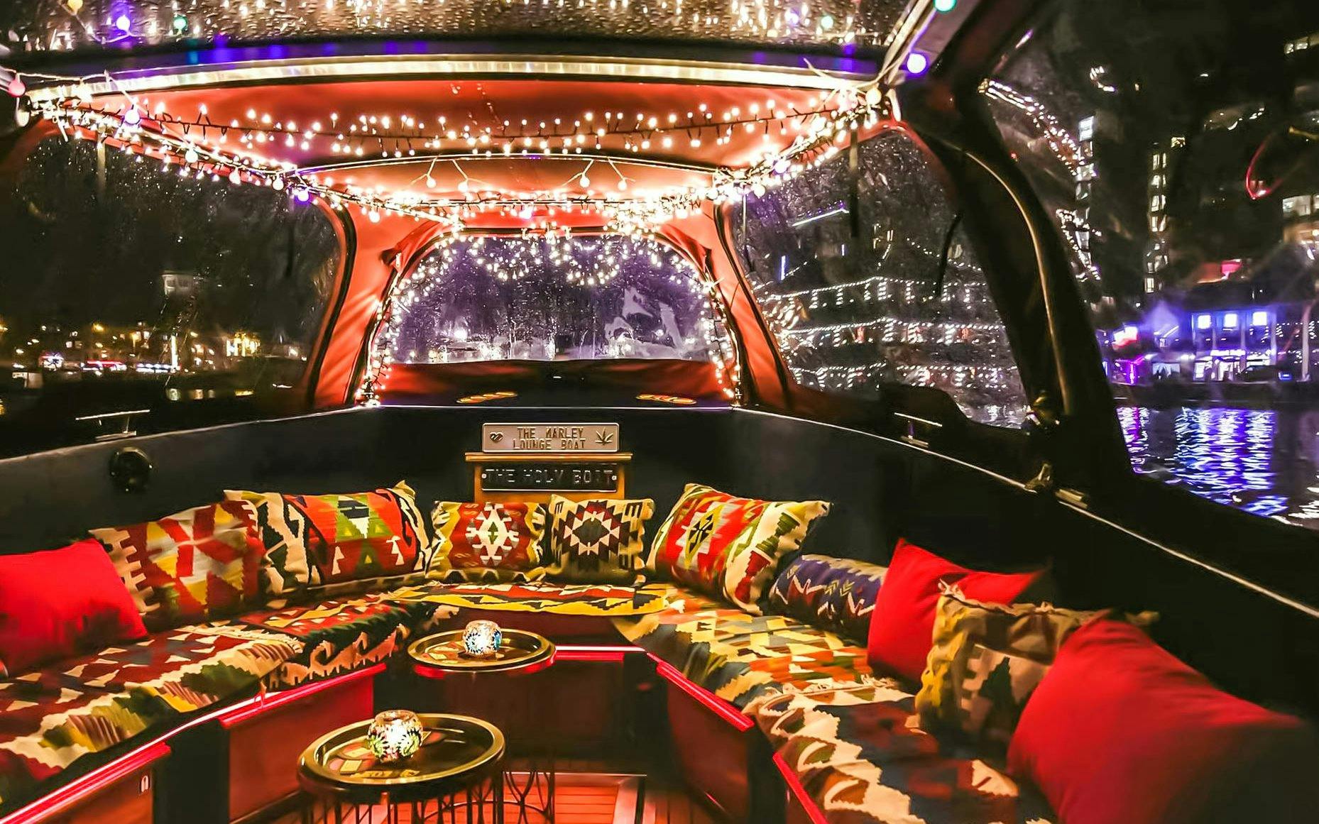 Heated lounge area with colorful cushions on a covered boat cruise in Amsterdam at night.