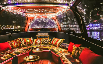 Heated lounge area with colorful cushions on a covered boat cruise in Amsterdam at night.