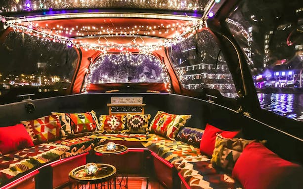 Heated lounge area with colorful cushions on a covered boat cruise in Amsterdam at night.