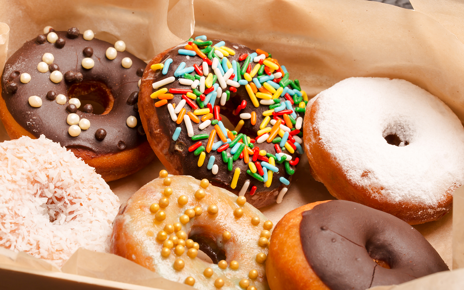 Donuts with colorful sprinkles and various toppings in a box.
