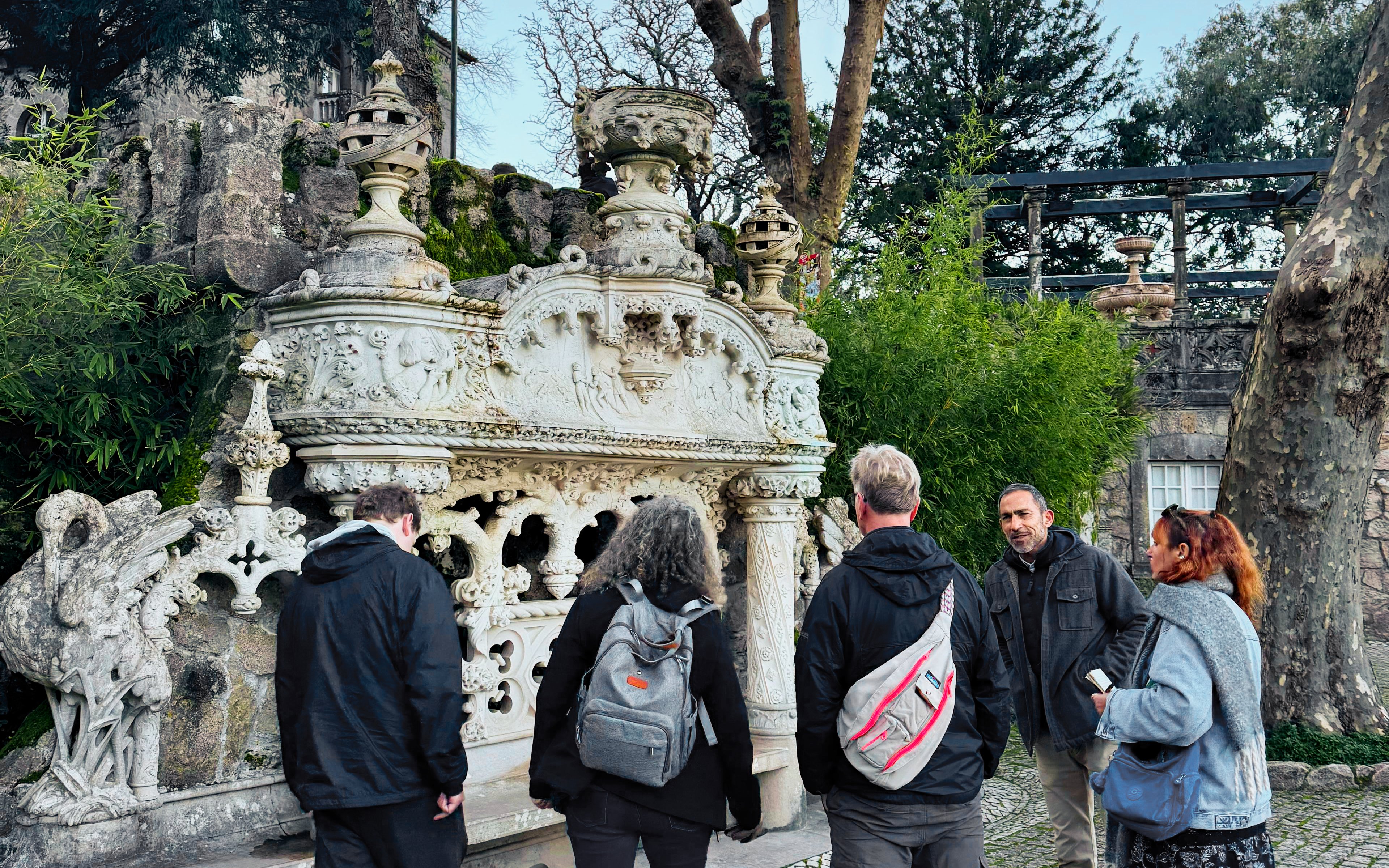 Tourists with guide at ornate stone structure in Quinta da Regaleira, Sintra.