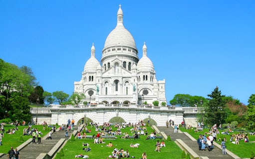 Sacré-Cœur Basilica in Montmartre, Paris with visitors on the steps and lawn.
