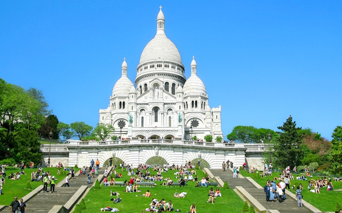 Sacré-Cœur Basilica in Montmartre, Paris with visitors on the steps and lawn.