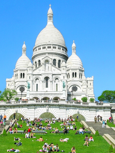 Sacré-Cœur Basilica in Montmartre, Paris with visitors on the steps and lawn.