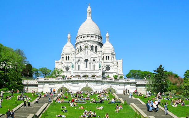 Sacré-Cœur Basilica in Montmartre, Paris with visitors on the steps and lawn.