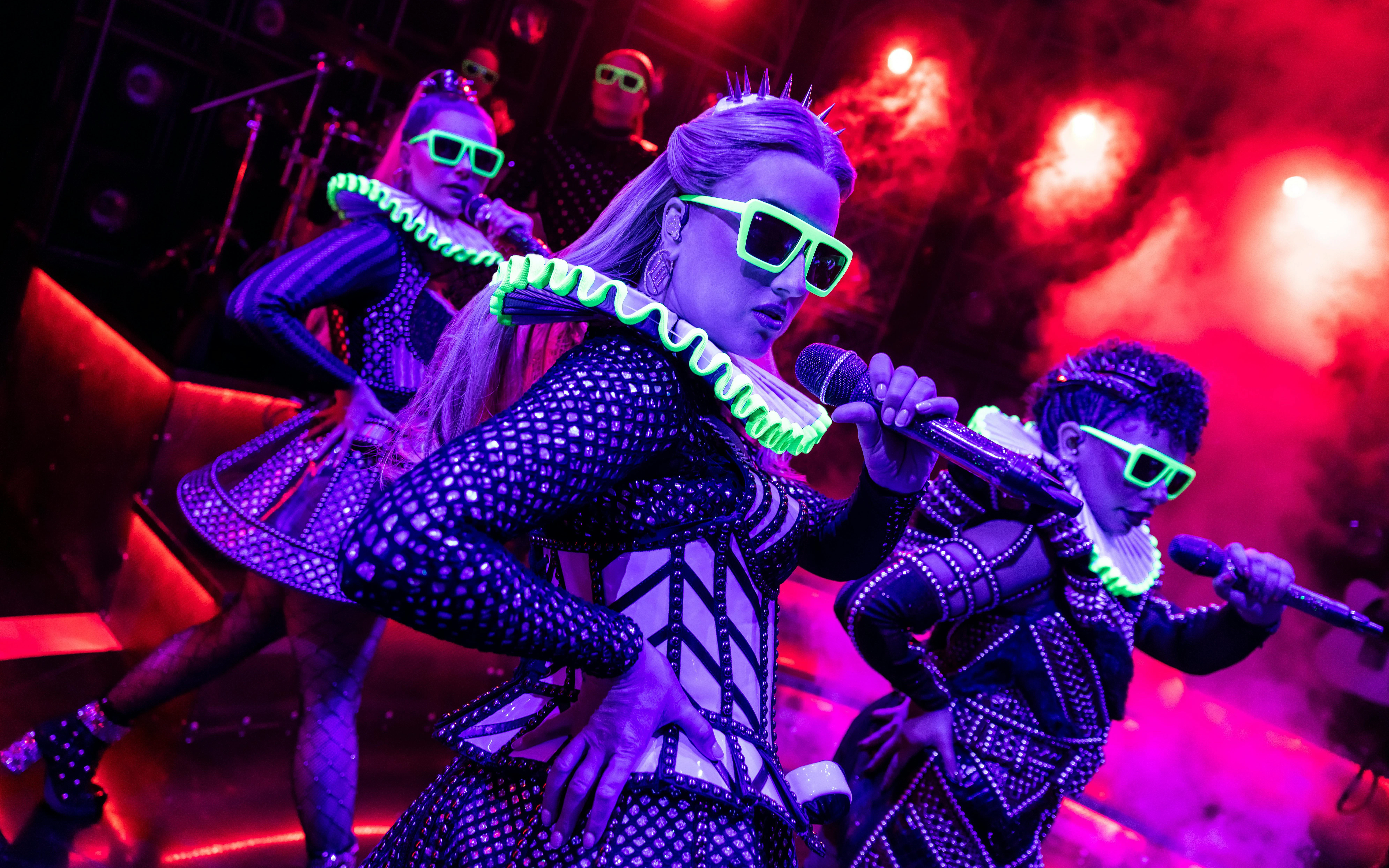 Performers in neon costumes singing on stage during Six musical in West End.