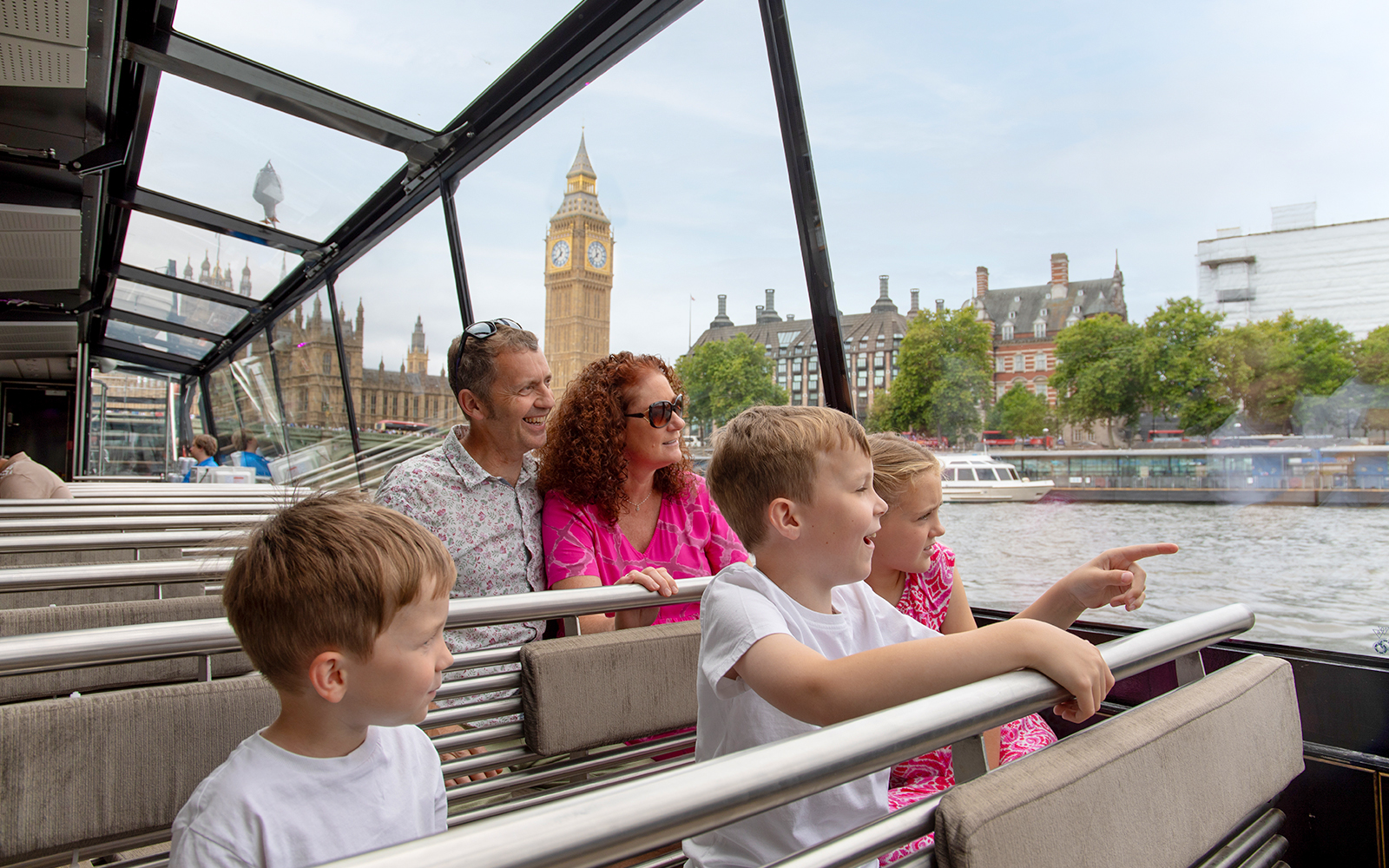 Family enjoying Thames river cruise with view of Big Ben, London.