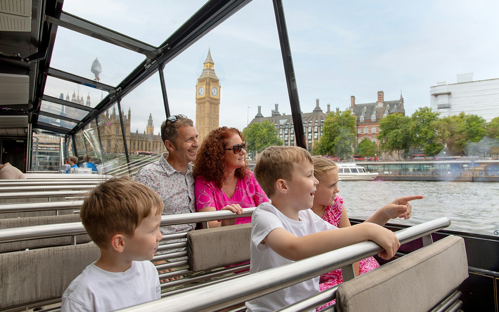 Family enjoying Thames river cruise with view of Big Ben, London.