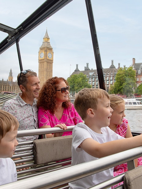 Family enjoying Thames river cruise with view of Big Ben, London.