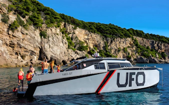 Boat tour with passengers near rocky cliffs in Dubrovnik.
