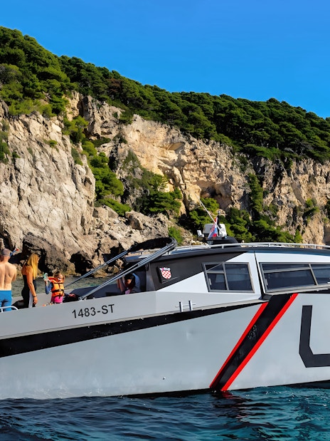 Boat tour with passengers near rocky cliffs in Dubrovnik.