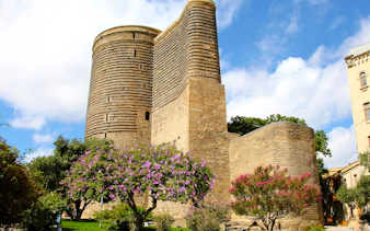 Maiden Tower in Baku surrounded by blooming trees.