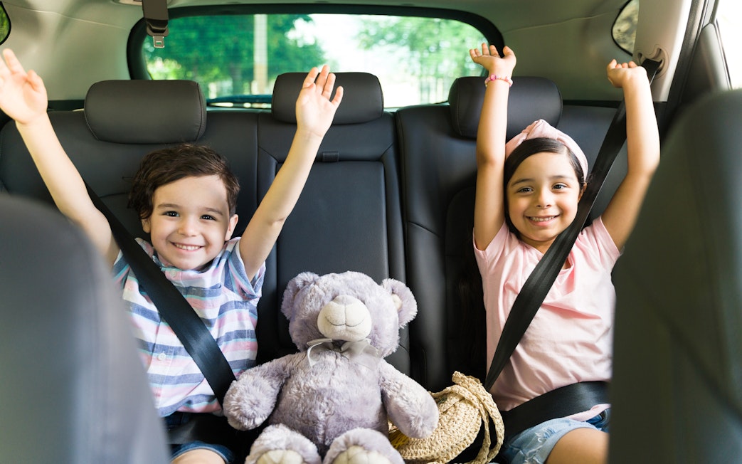 Children smiling in car seats with a teddy bear, heading to Andamanda Phuket Water Park.