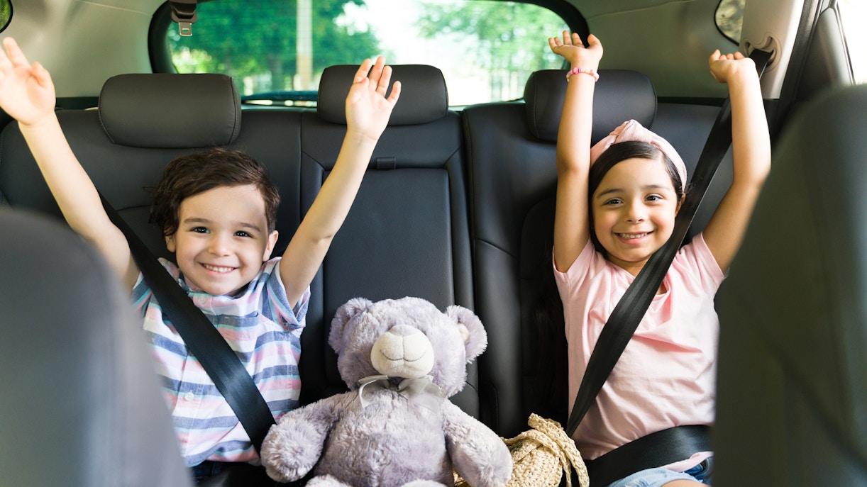 Children smiling in car seats with a teddy bear, heading to Andamanda Phuket Water Park.