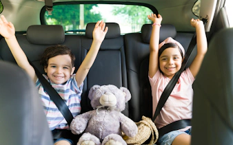 Children smiling in car seats with a teddy bear, heading to Andamanda Phuket Water Park.