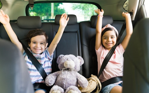 Children smiling in car seats with a teddy bear, heading to Andamanda Phuket Water Park.