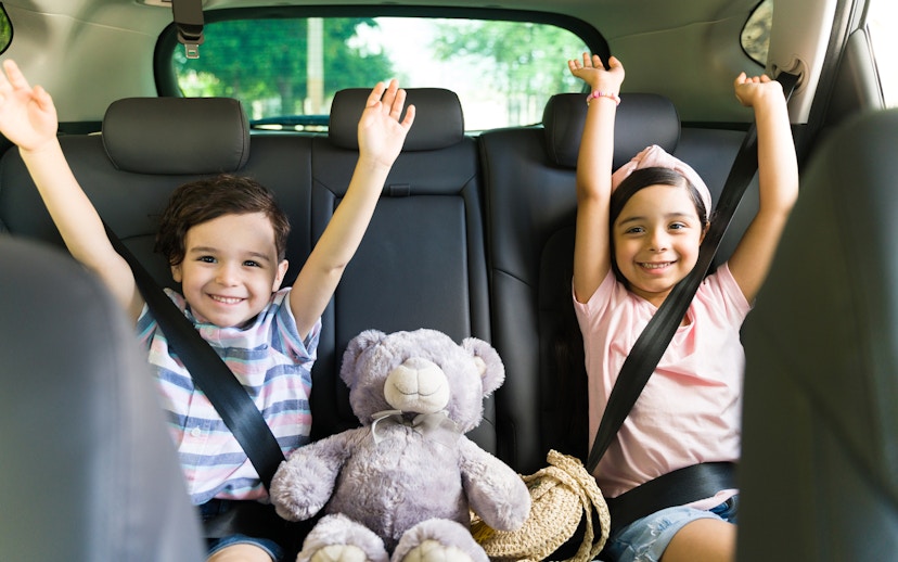 Children smiling in car seats with a teddy bear, heading to Andamanda Phuket Water Park.