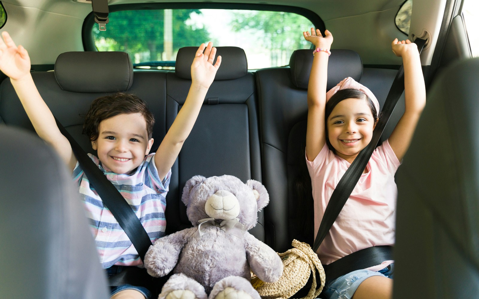 Children smiling in car seats with a teddy bear, heading to Andamanda Phuket Water Park.
