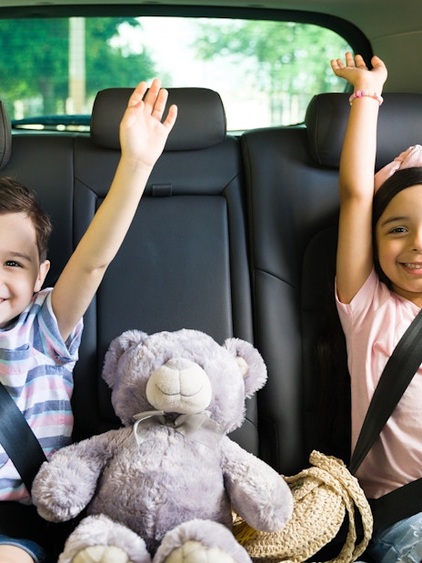 Children smiling in car seats with a teddy bear, heading to Andamanda Phuket Water Park.