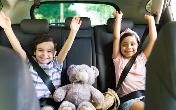 Children smiling in car seats with a teddy bear, heading to Andamanda Phuket Water Park.