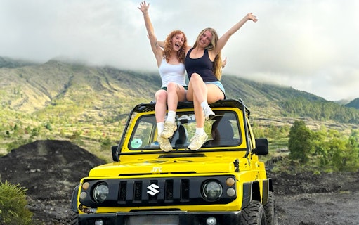Two people sitting on a yellow jeep with Mount Batur in the background, Bali.