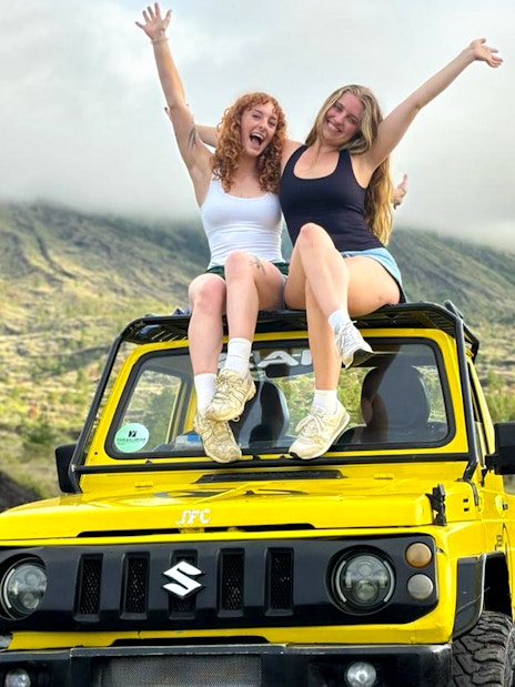 Two people sitting on a yellow jeep with Mount Batur in the background, Bali.