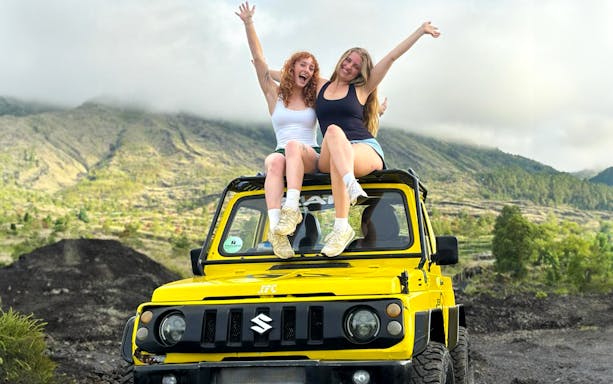 Two people sitting on a yellow jeep with Mount Batur in the background, Bali.