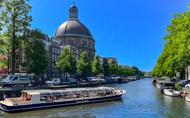 Canal cruise boat on Amsterdam canal with historic buildings and dome in the background.