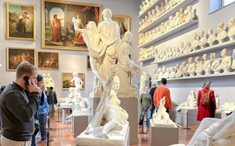 Visitors using audio guides at Academia Gallery, Florence, surrounded by classical sculptures and paintings.