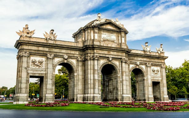 Puerta de Alcalá in Madrid, near Prado Museum, surrounded by gardens.