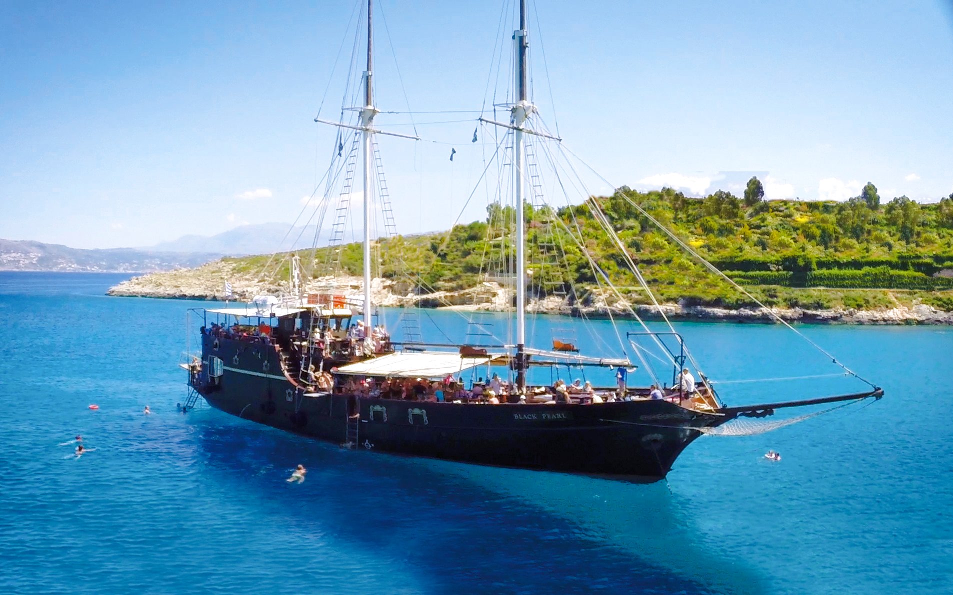 Pirate ship cruising in Souda Bay with swimmers nearby, Crete, Greece.
